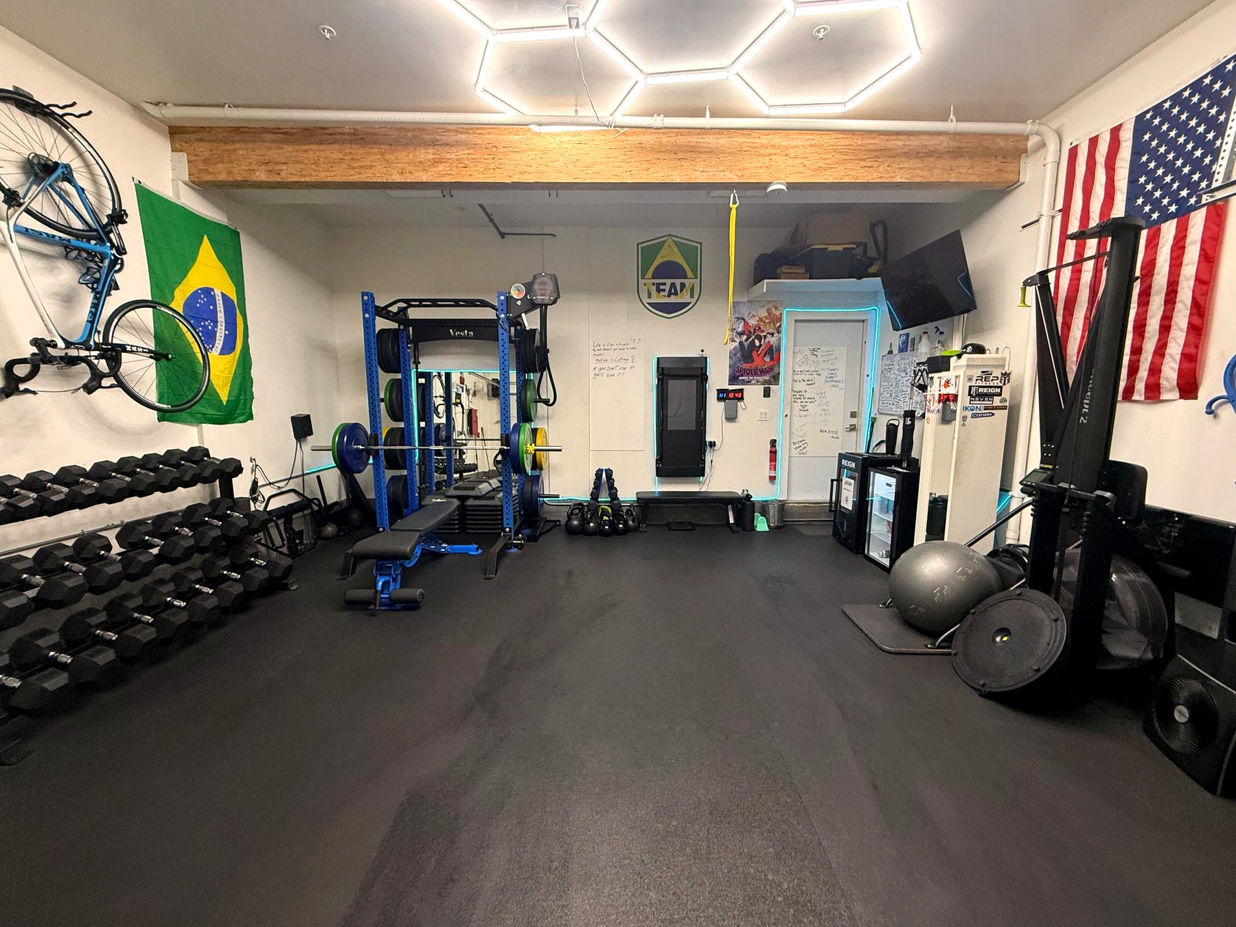 Inside ATeam Fitness studio — full overview with hex lighting, racks, dumbbells, Brazilian and American flags